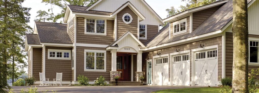 Two-story shake-sided home with white trim, a round window and a three-car garage