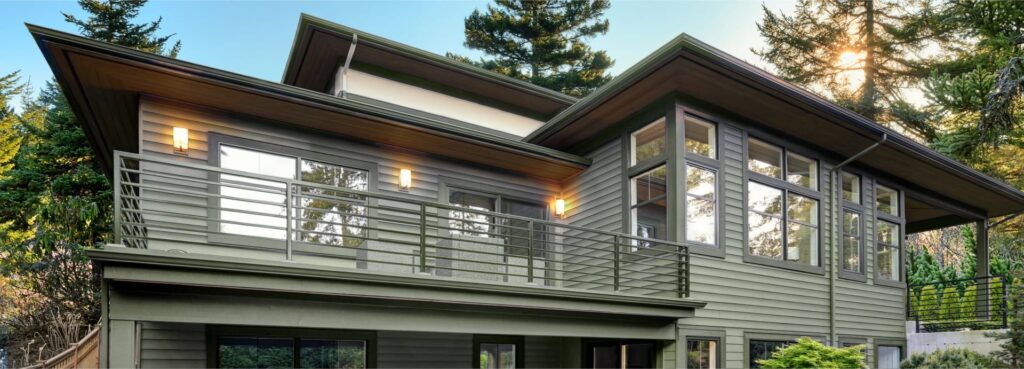 Contemporary two-story home with sage green lap siding, large windows and a wraparound deck
