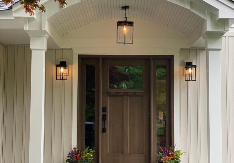Elegant front door with porch lights and potted plants in a modern home.