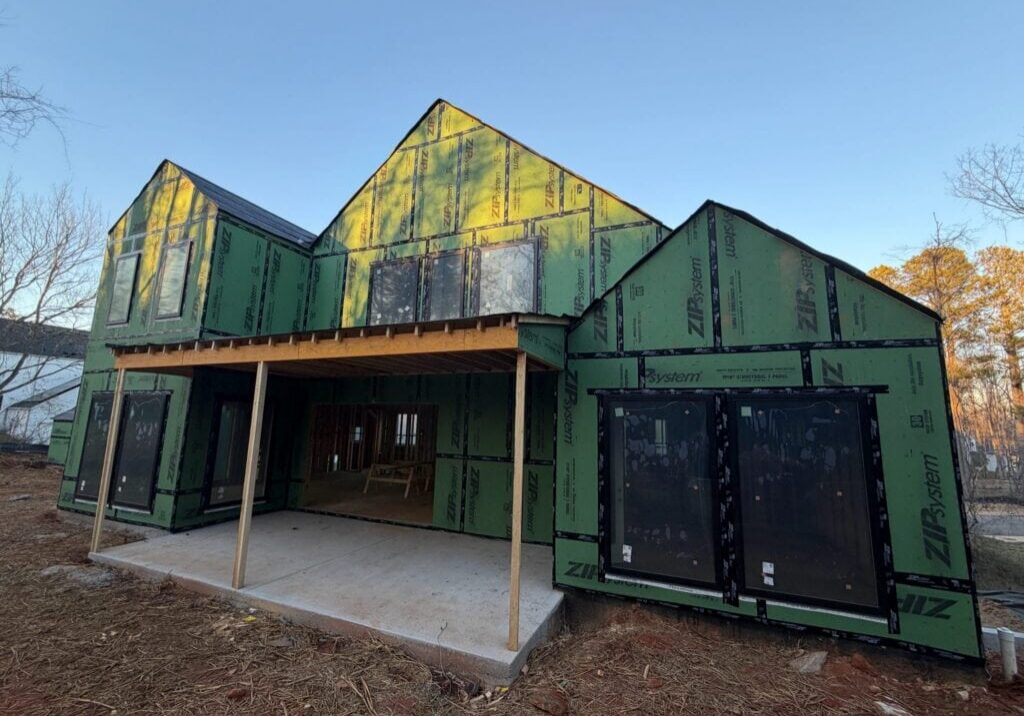 New home under construction with green ZIP System sheathing, large black-framed windows and a covered back patio